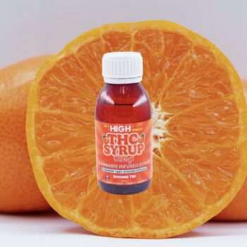 A bottle of Sky High Edibles THC Syrup – Orange 3000mg placed in front of a fresh, sliced orange on a plain white background.